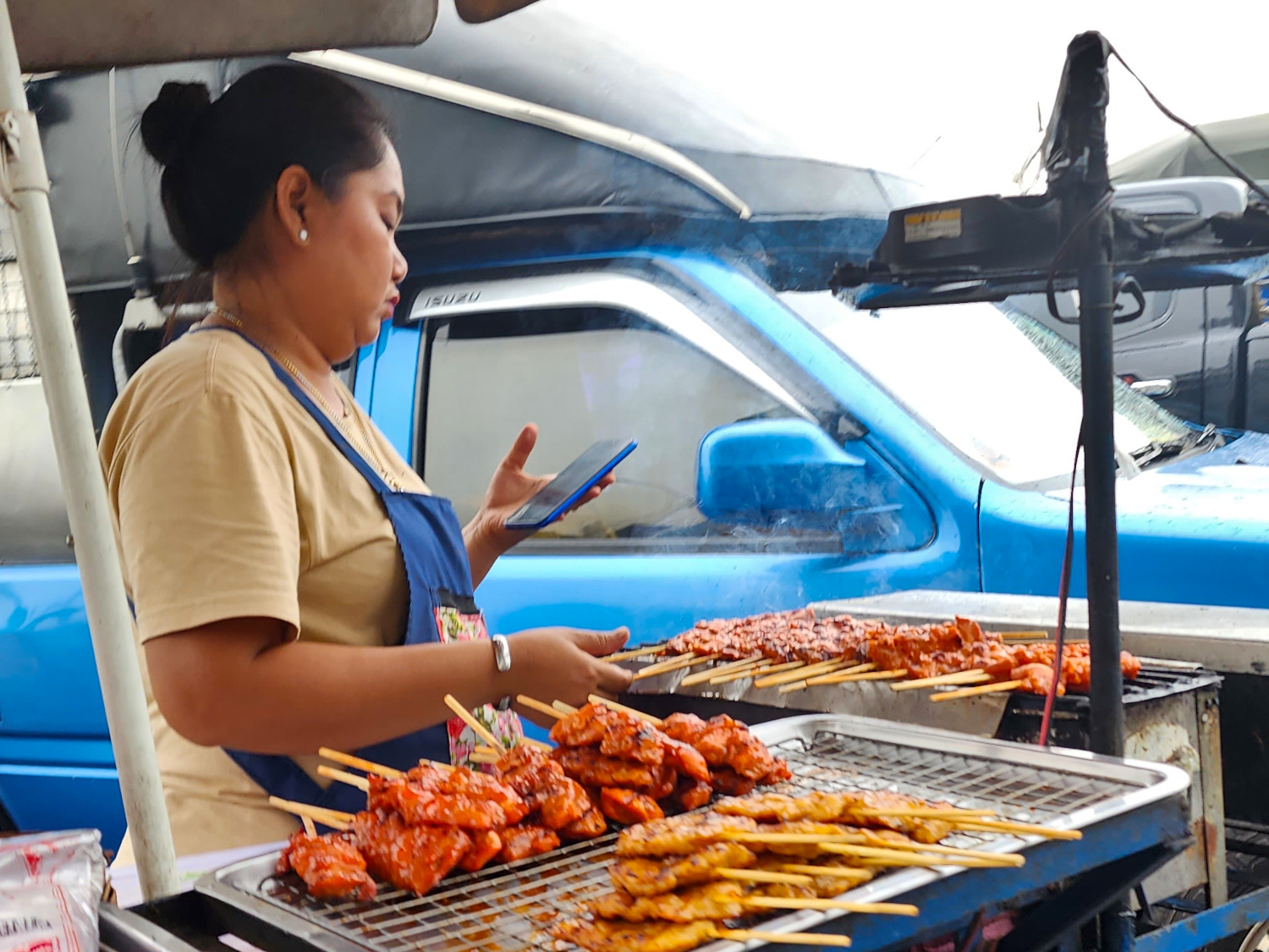 vendor texting while preparing ka-bobs street side Bangkok, Thailand