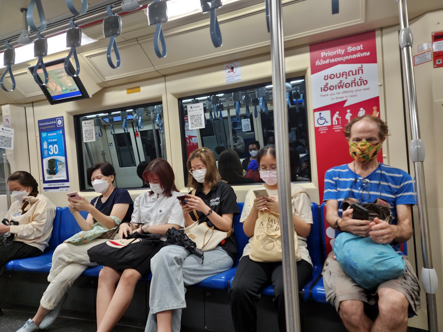 tourist texting along with the locals on the train in Bangkok, Thailand