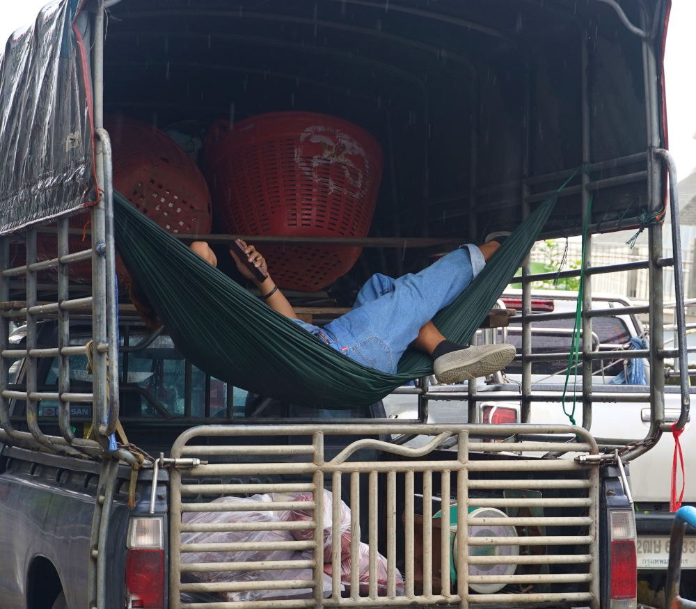a man hanging in a hammock in the rear of his truck on the streets Bangkok, Thailand