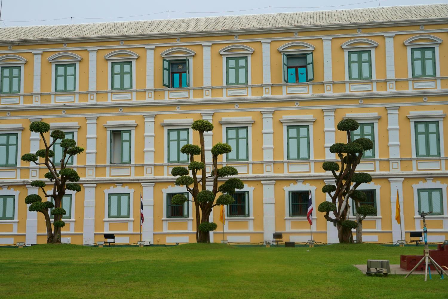 perfectly manicured lawn and topiary before the bright yellow Ministry of Defense building, Bangkok, Thailand